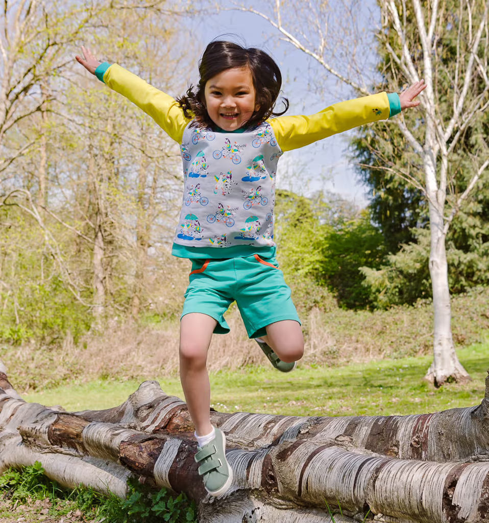 Child jumping on a log in a park with trees and grass in the background