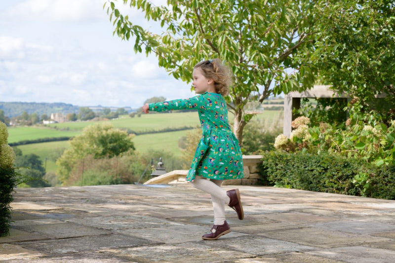 Image of girl running outside, wearing a Ducky Zebra green dress with a fun print of hedgehogs and dogs gardening