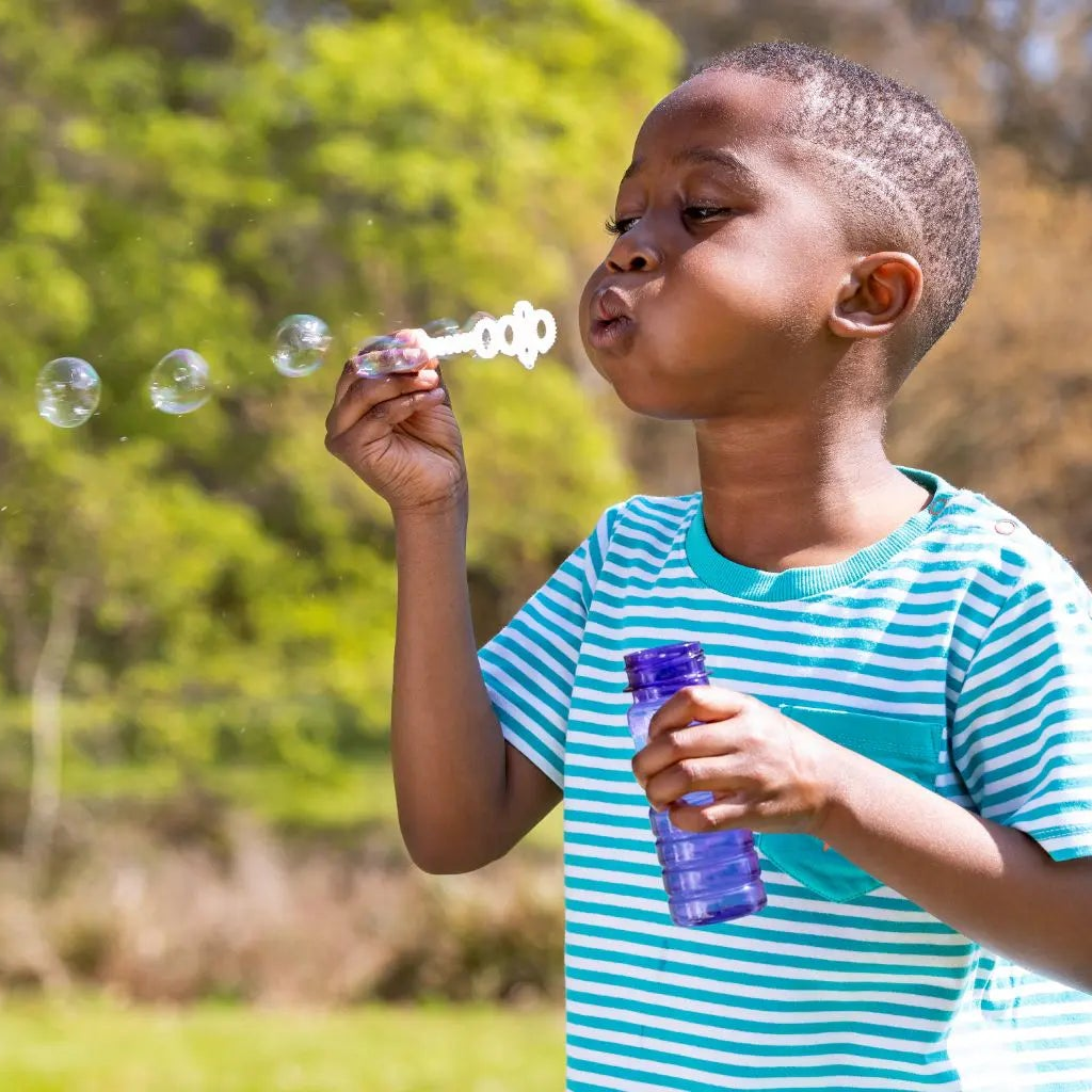 Child blowing bubbles in a park with trees and grass in the background