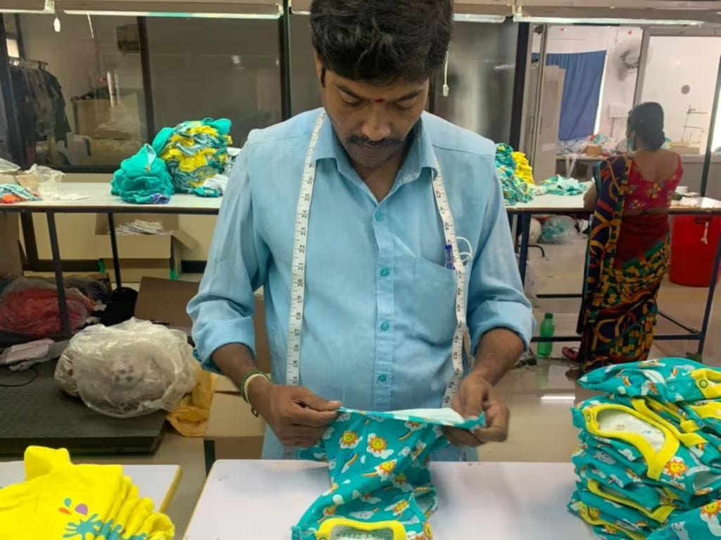 Man measuring fabric in a workshop setting with stacks of colorful fabric around him.