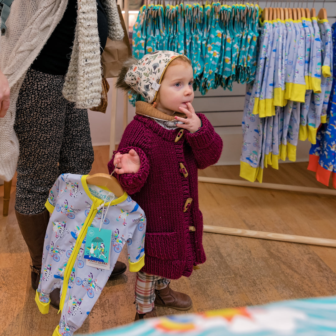Child in a store looking at children's clothing with a tag on a hanger.