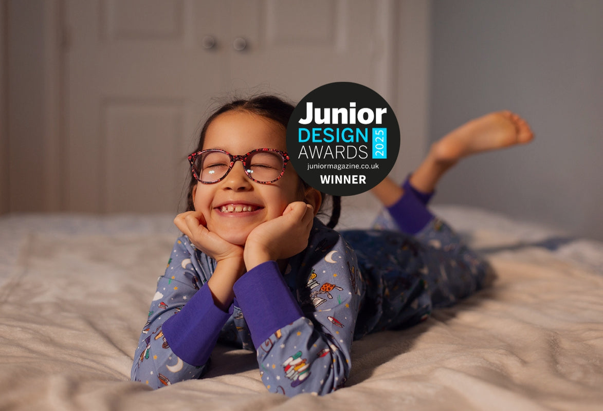 Child wearing Ducky Zebra x Roald Dahl pyjamas, lying on a bed with Junior Design Awards logo
