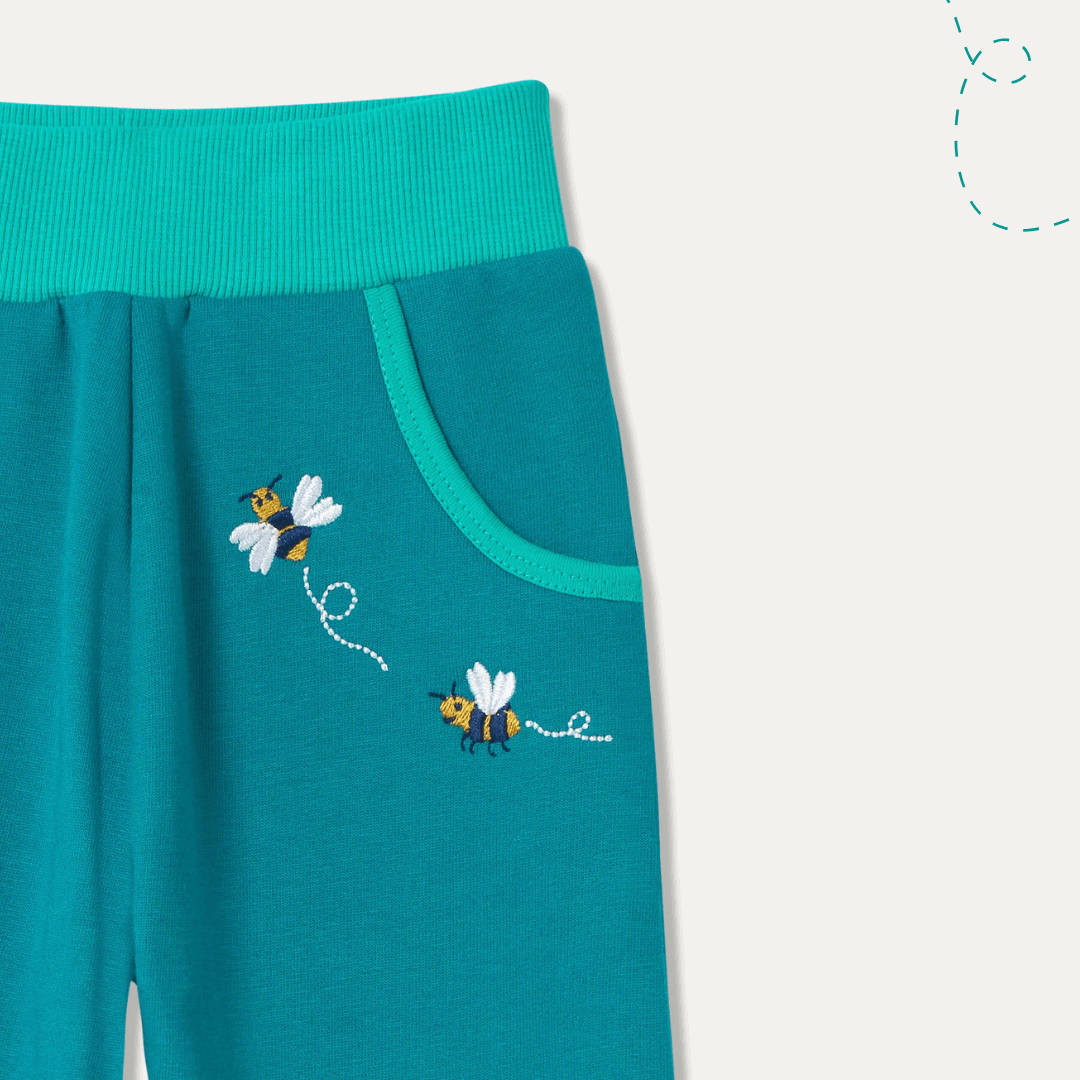 Teal pants with embroidered bees on a white background