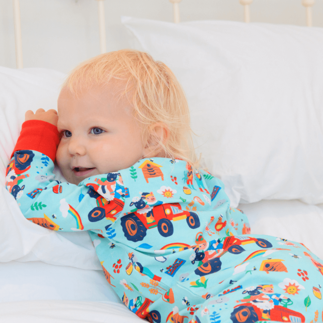 Child wearing a colorful outfit with vehicle pattern lying on a bed.
