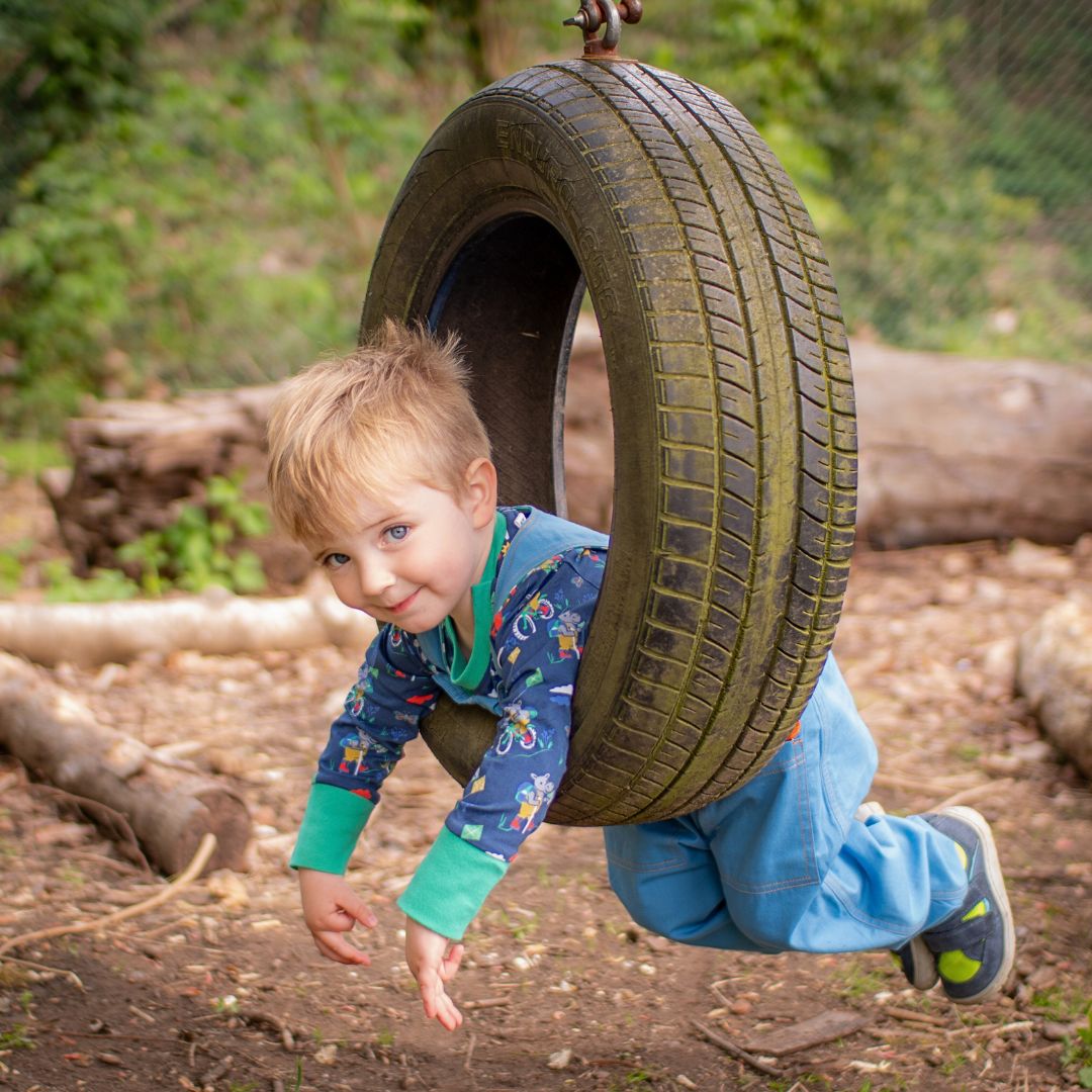 Boy lying on a tire swing, wearing a Ducky Zebra blue top and dungarees