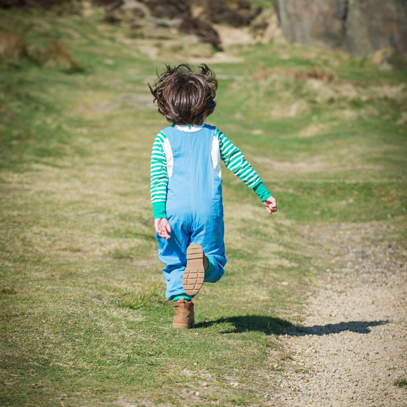 The back of a child running, wearing blue dungarees and a long sleeve top with green and white stripes