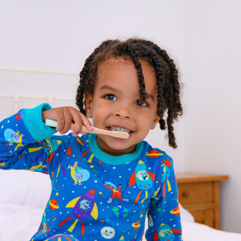 Image of a boy brushing his teeth wearing Ducky Zebra sustainable pyjamas, with a fun space print. 