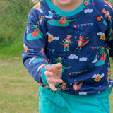 Close up of child wearing a Ducky Zebra sweatshirt and cords. The jumper is blue with a fun print of a cheetah, fox, duck and crocodile playing music together. The jumper has a festival vibe. It has two orange buttons on the shoulder for easy dressing and contrasting turquoise cuffs.