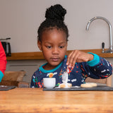Girl concentrating on baking, while wearing a fun Ducky Zebra sweatshirt with a blue background and fun festive print.