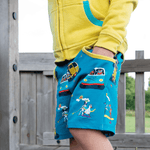Child wearing a yellow hoodie and teal shorts with a campervan and paddleboard print, yellow waistband and two big pockets