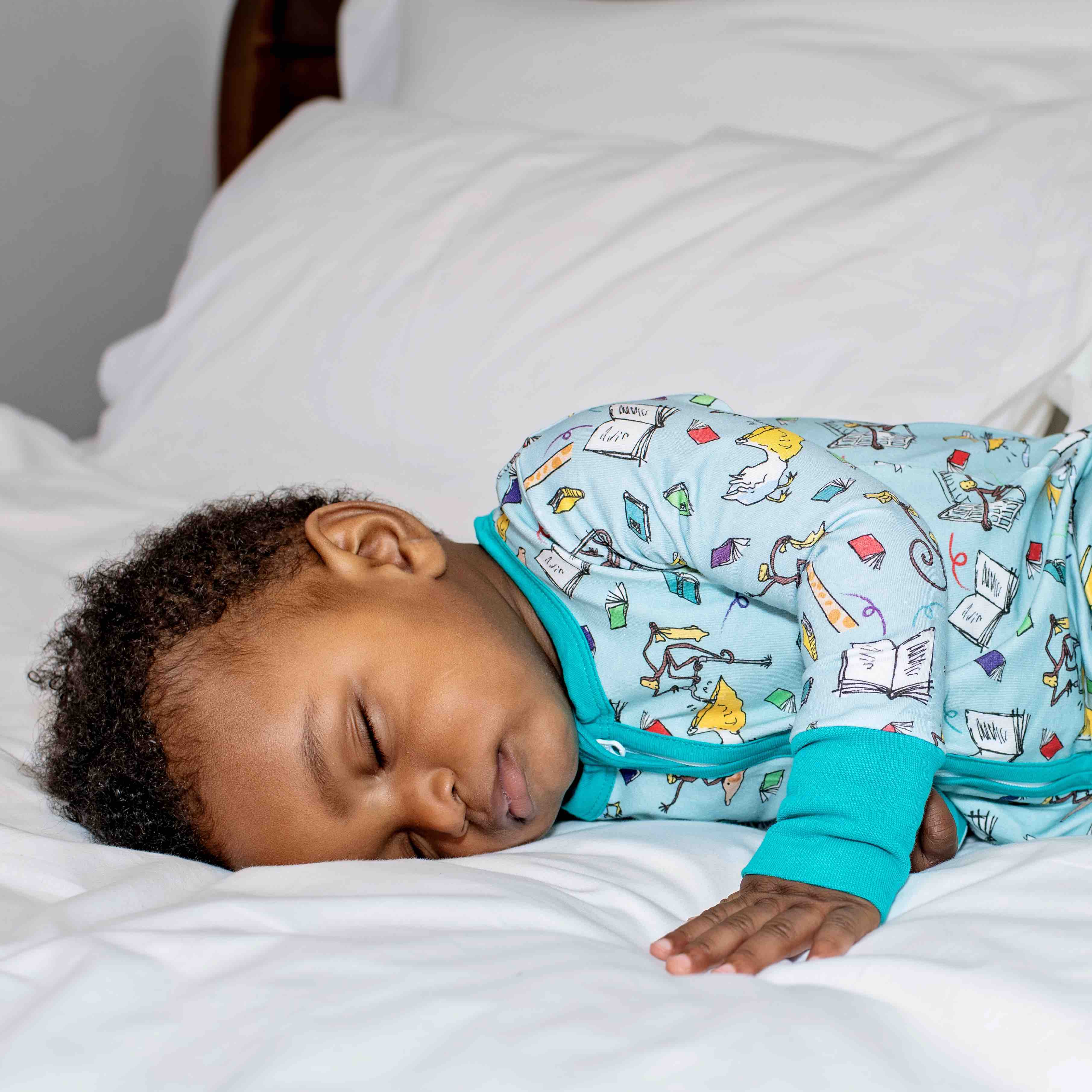 Cute sleeping baby, wearing a Ducky Zebra x Roald Dahl zip-up sleesuit, with a fun print featuring characters from "The Giraffe and the Pelly and Me" leaping from the pages. 