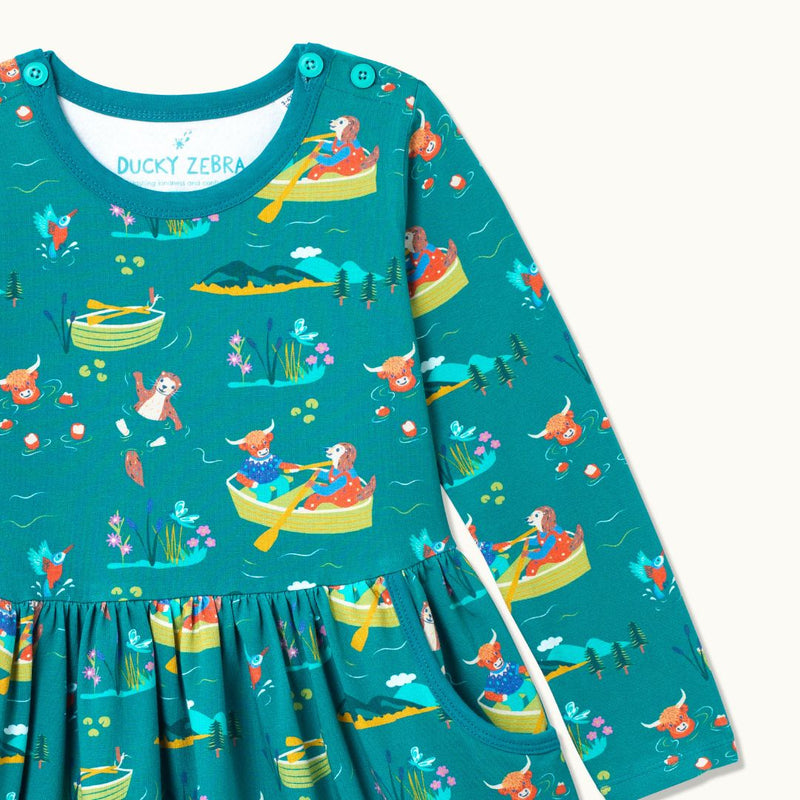 Close up of teal Skater Dress with repeat print pattern of a highland cow, otter and king fisher rowing, wild swimming and exploring together. The dress has buttons on the neck for easy dressing