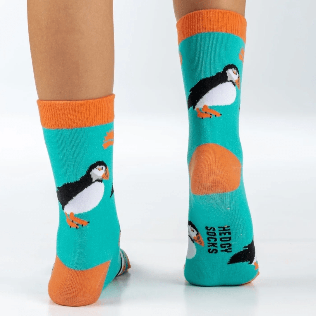 Child wearing turquoise socks, with orange toes and trim and a repeat puffin print