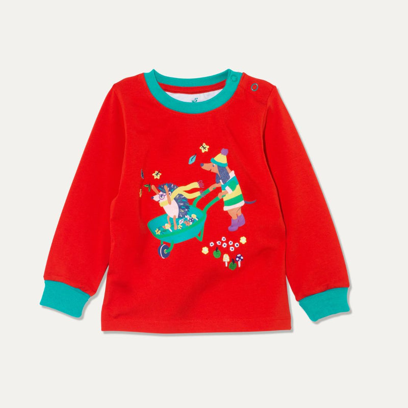 Long sleeve kids' red t-shirt with a print of a dog and hedgehog playing with leaves and a wheelbarrow. The red top has a contrasting turquoise neck rib and cuffs, and has turquoise poppers on one shoulder for easy dressing.
