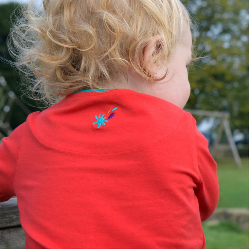 The back of a toddler wearing a red Ducky Zebra top. The top has an embroidered splash power button.