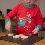 Image of child making biscuits while wearing a red Ducky Zebra top with a hedgehog and dog playing in a wheelbarrow. The red top has turquoise cuffs.