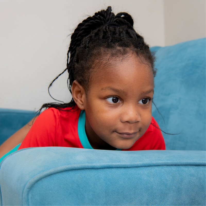 Image of a child lying on a blue sofa wearing a Ducky Zebra red top with a turquoise trim.