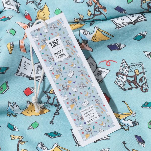 Close up of organic cotton PJs, showing a bookmark swingtag and characters from the Giraffe and the Pelly and Me leaping from the pages of a book