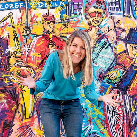 Image of Sally, founder of Ducky Zebra, smiling, with her hands out and open, in front of a brightly painted wall 