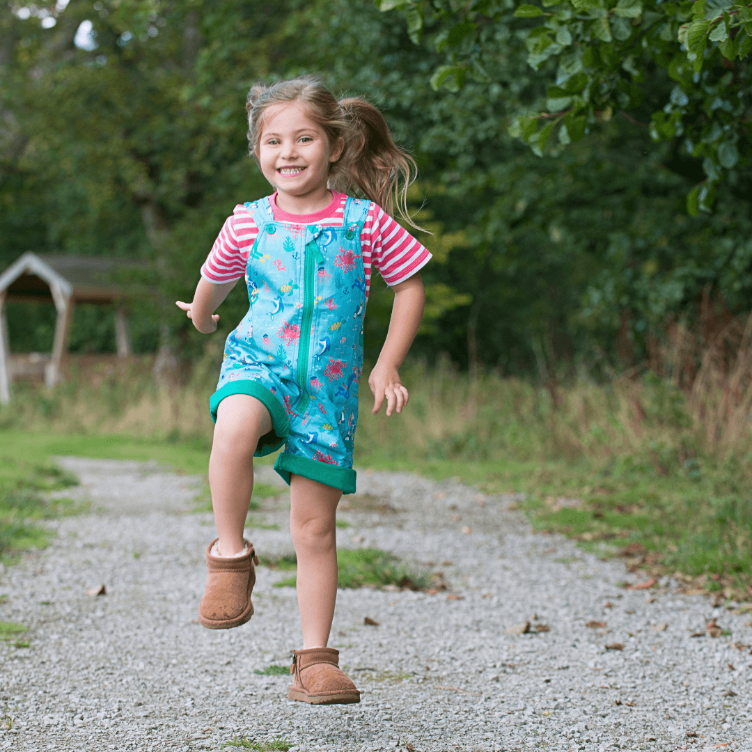 Girl smiling at the camera wearing Ducky Zebra short dungarees with a green zip