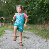 Girl smiling at the camera wearing Ducky Zebra short dungarees with a green zip