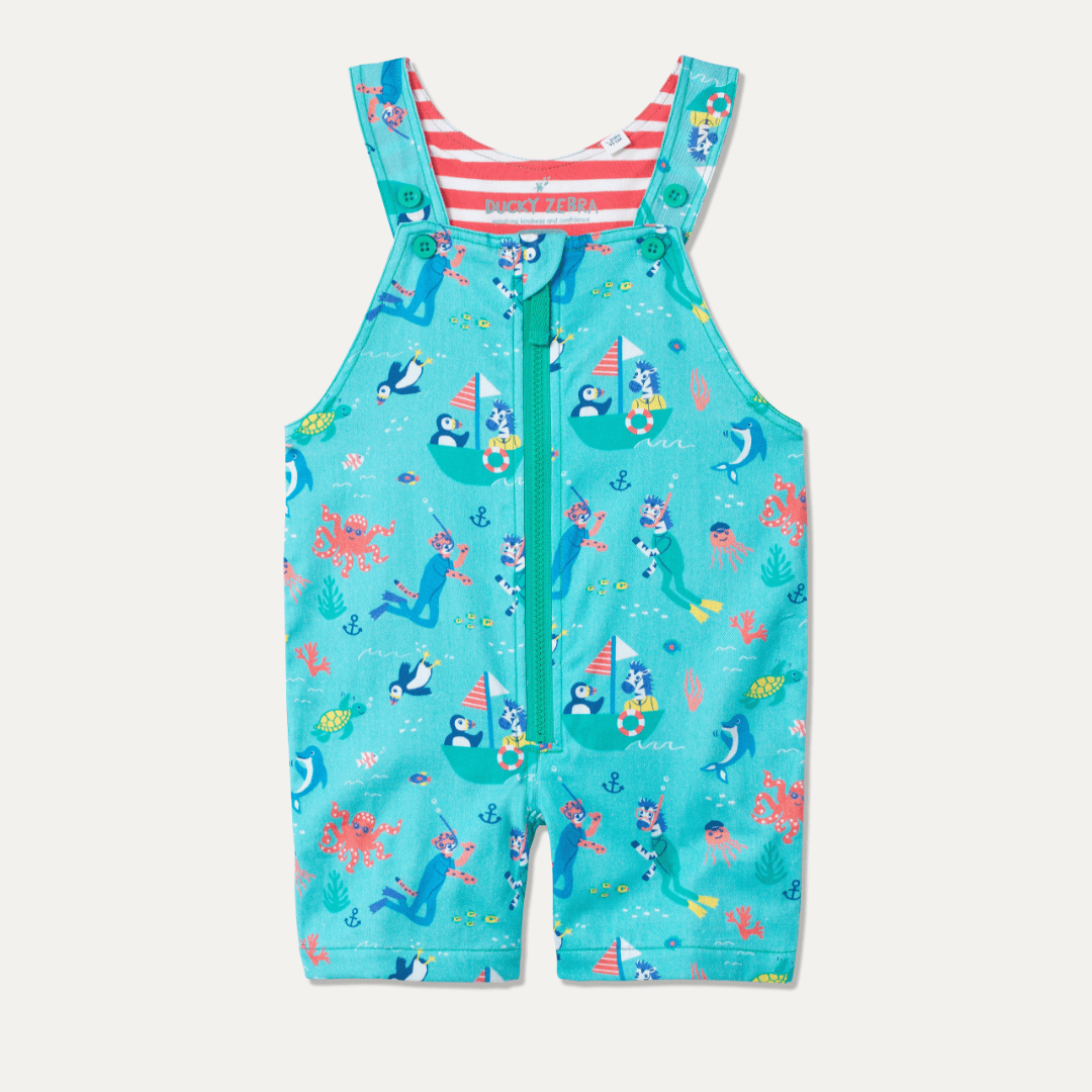 Children's blue short dungarees with a green zip and an ocean-themed print - including a sailing puffin and zebra, and a scuba diving cheetah and zebra