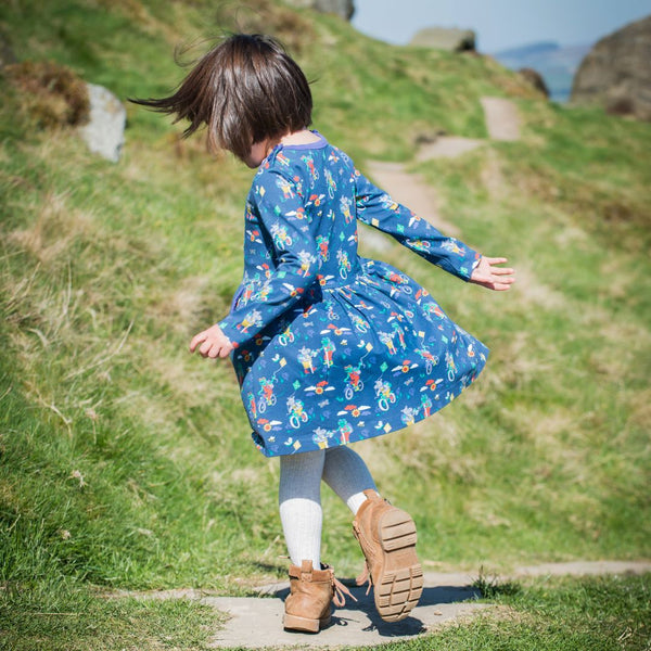 Girl spinning in a Ducky Zebra blue dress with print of frogs and hippos walking and cycling. The girl is outside on the Yorkshire Moors