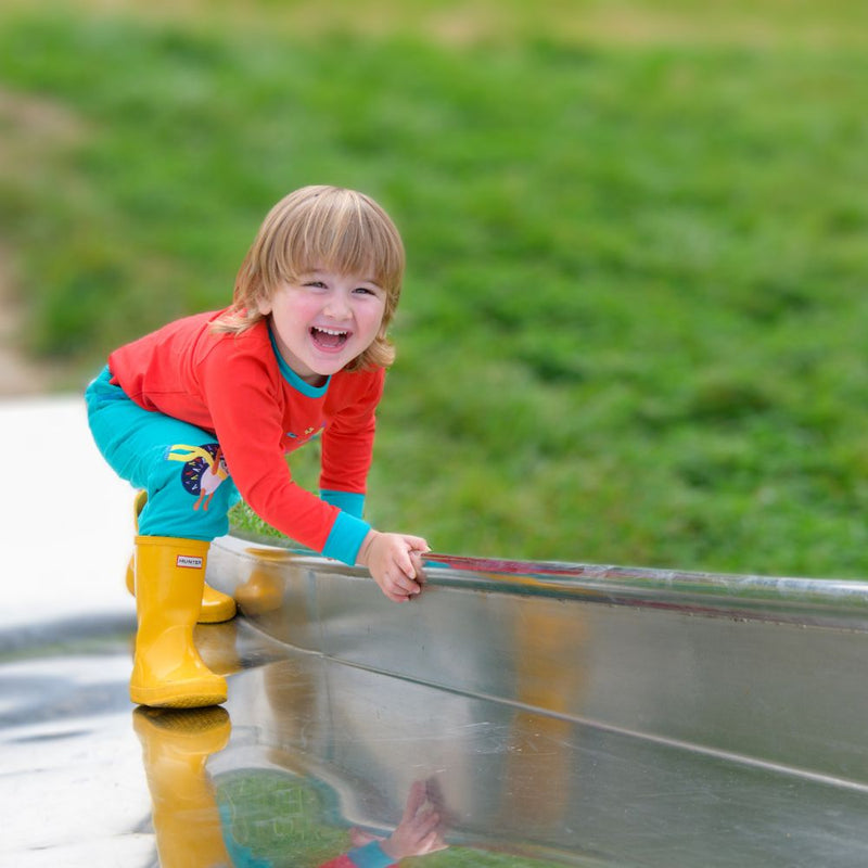 Smiling boy climbing up a slide, wearing a red Ducky Zebra top and turquoise cords