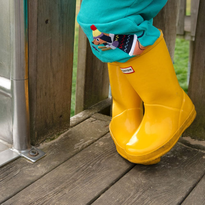 Close up image of a child's leg. They're wearing yellow wellies and turquoise cords, with a fun dog appliqué poking out of the top of the wellie