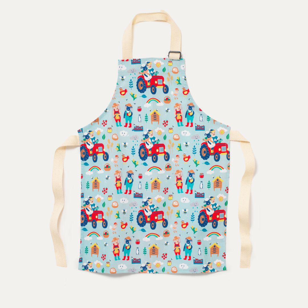 Children's apron with light turquoise background and fun farmyard print with tractors, pigs and sheep