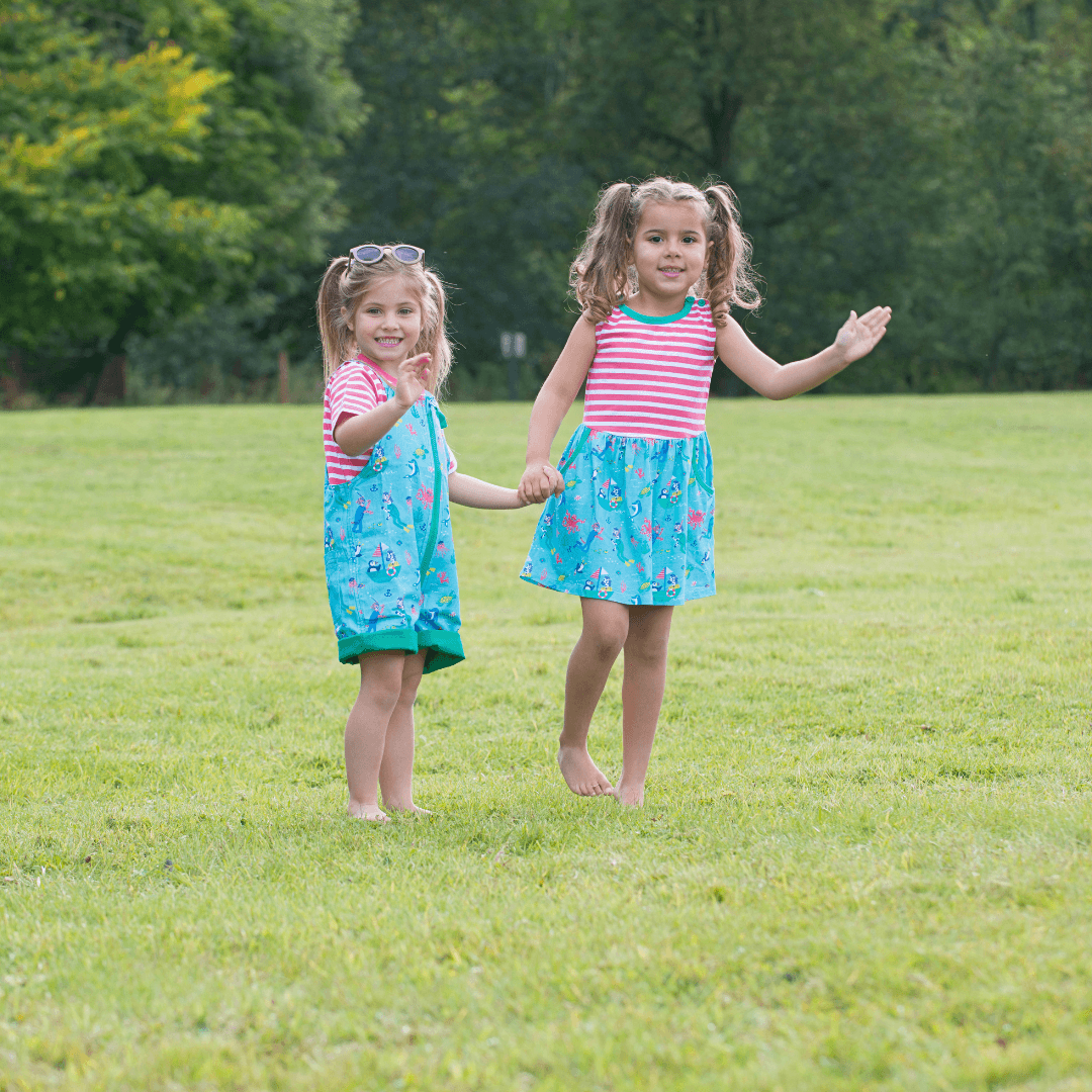Two children waving at the camera wearing Ducky Zebra 'under the sea' nautical themed dress and dungarees