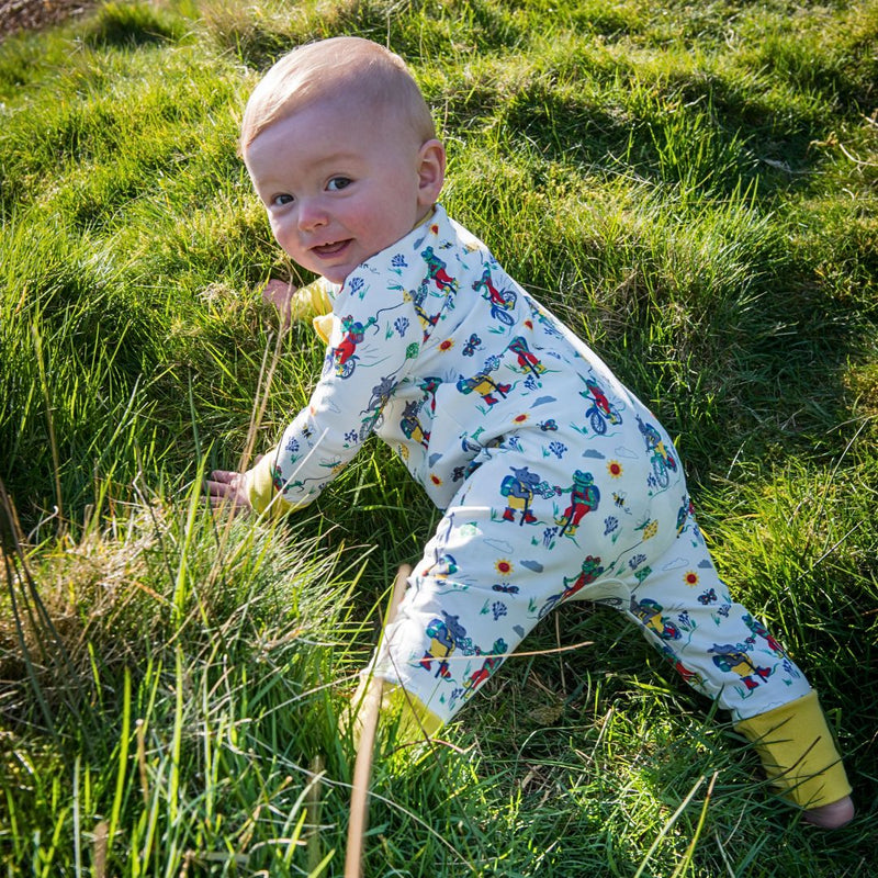 Smiling baby on the Yorkshire Moors wearing a cream Ducky Zebra romper with a repeat print pattern of frogs, hippos and bees walking and cycling on the Moors