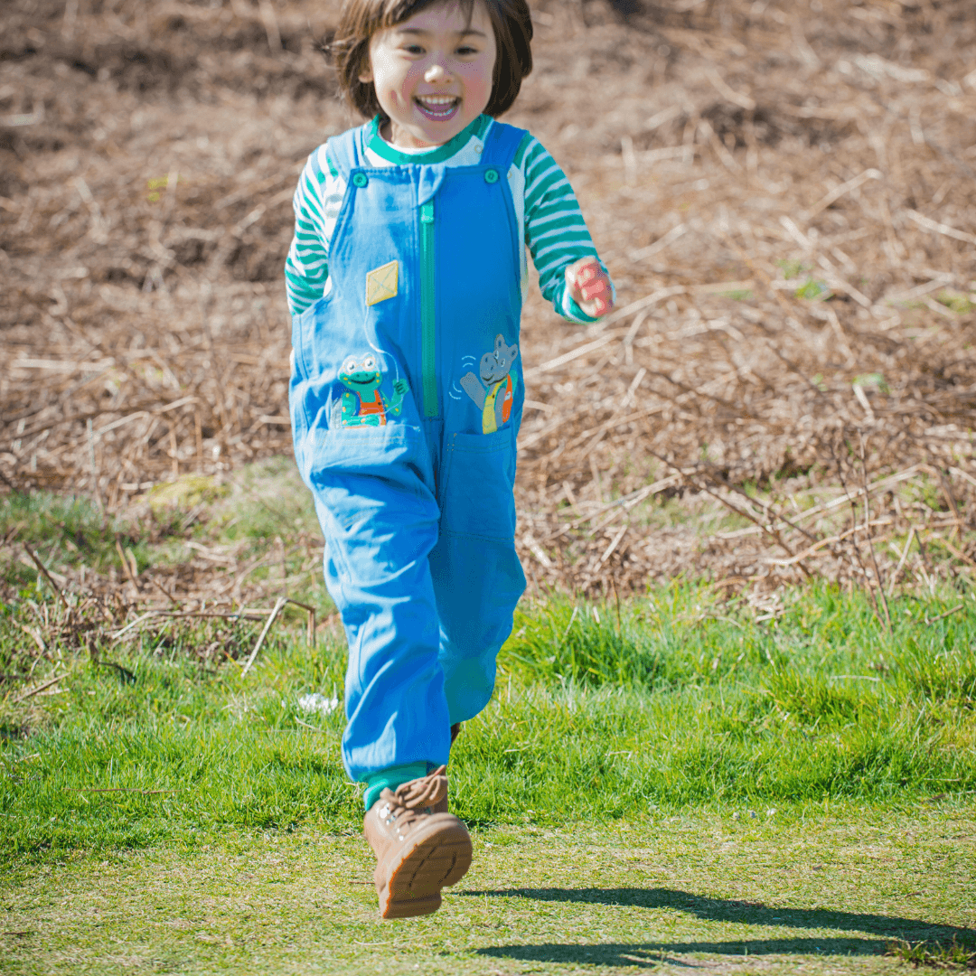 Child running outdoors in a blue outfit with a green background