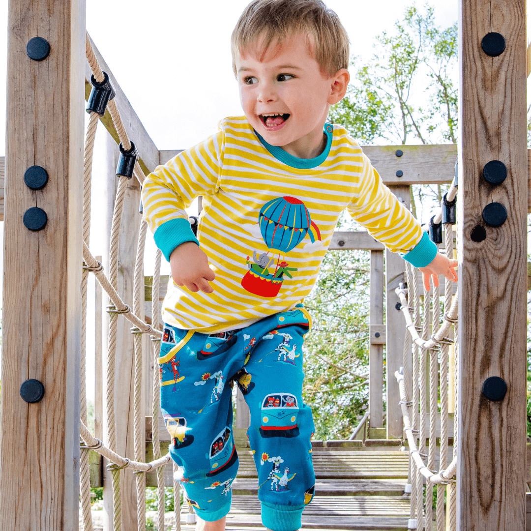 Child playing on a playground structure wearing a yellow and blue striped shirt with hot air balloon design.