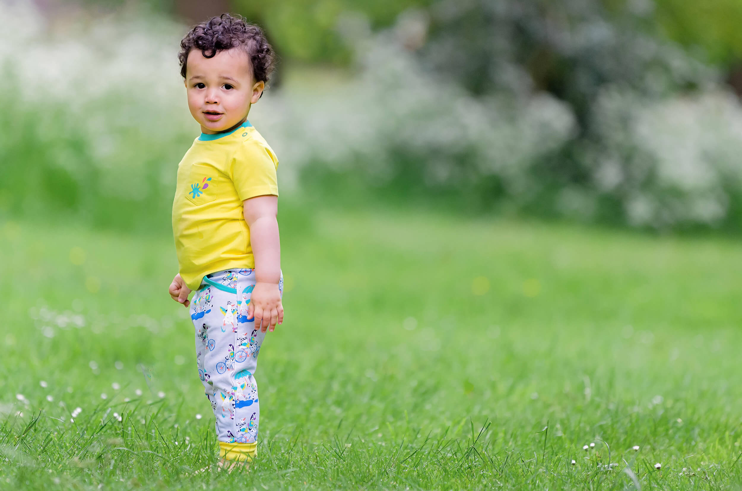 Child in a yellow shirt and patterned pants standing on grass