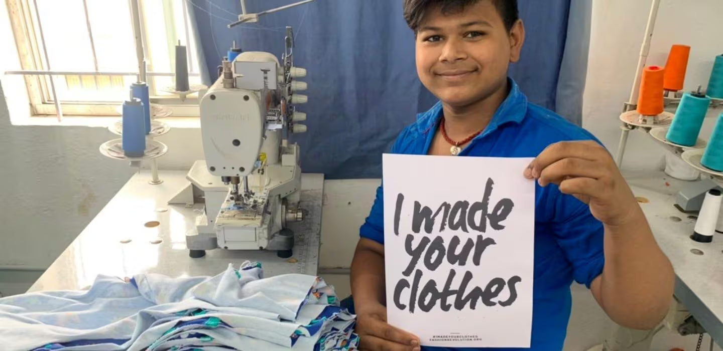 Child holding a sign saying 'I made your clothes' in a sewing workshop.