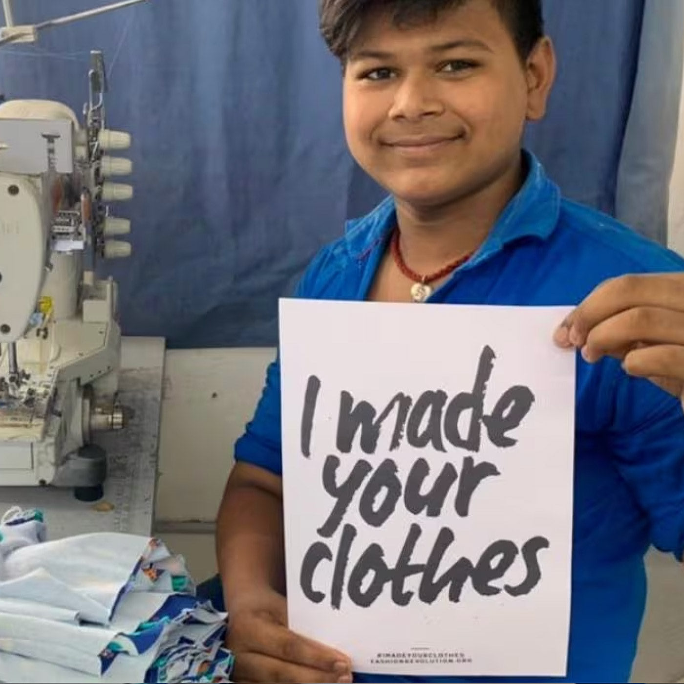 Man holding a sign saying 'I made your clothes' in a garment factory setting