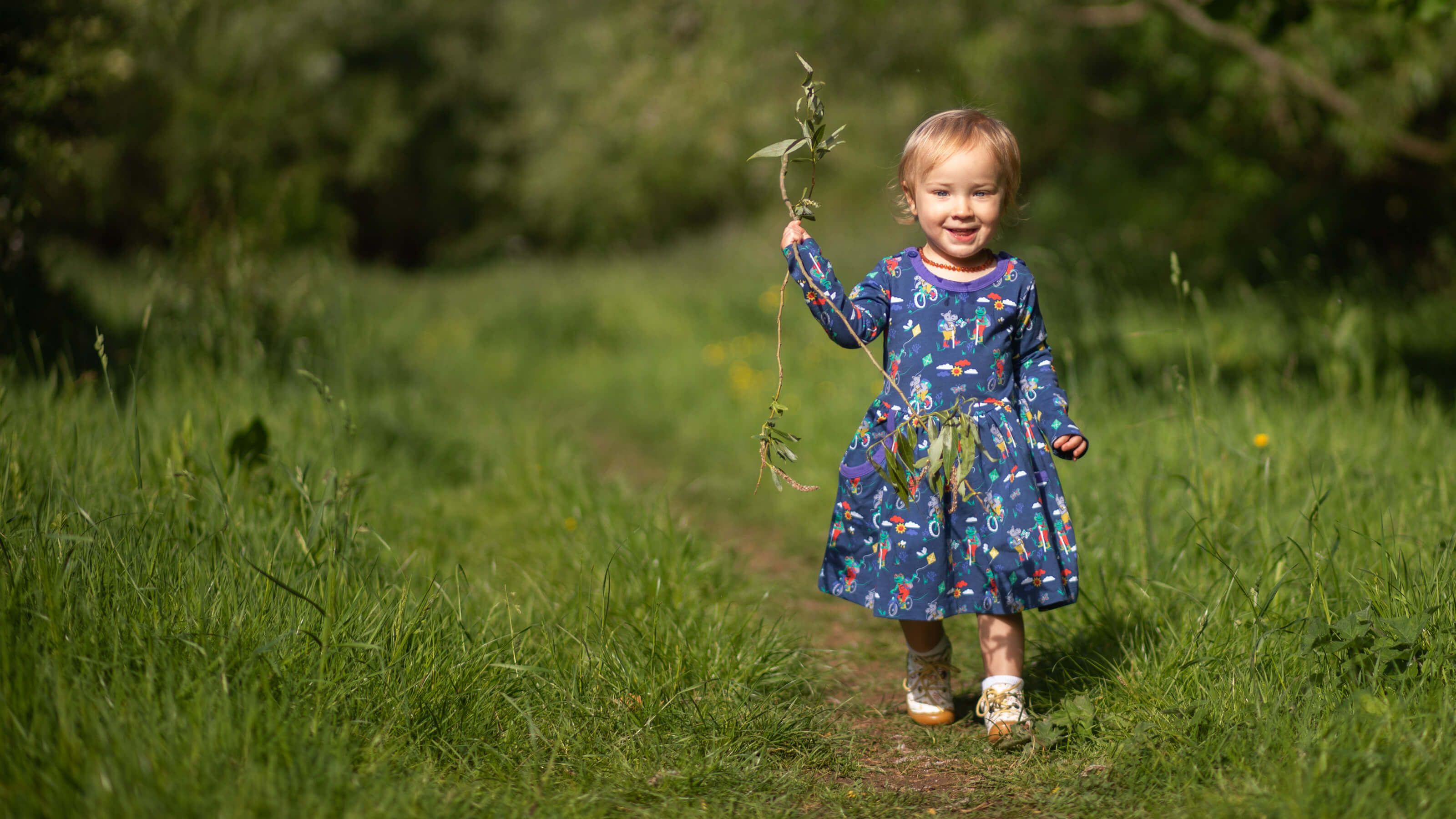 Child in a blue dress holding leaves in a grassy field