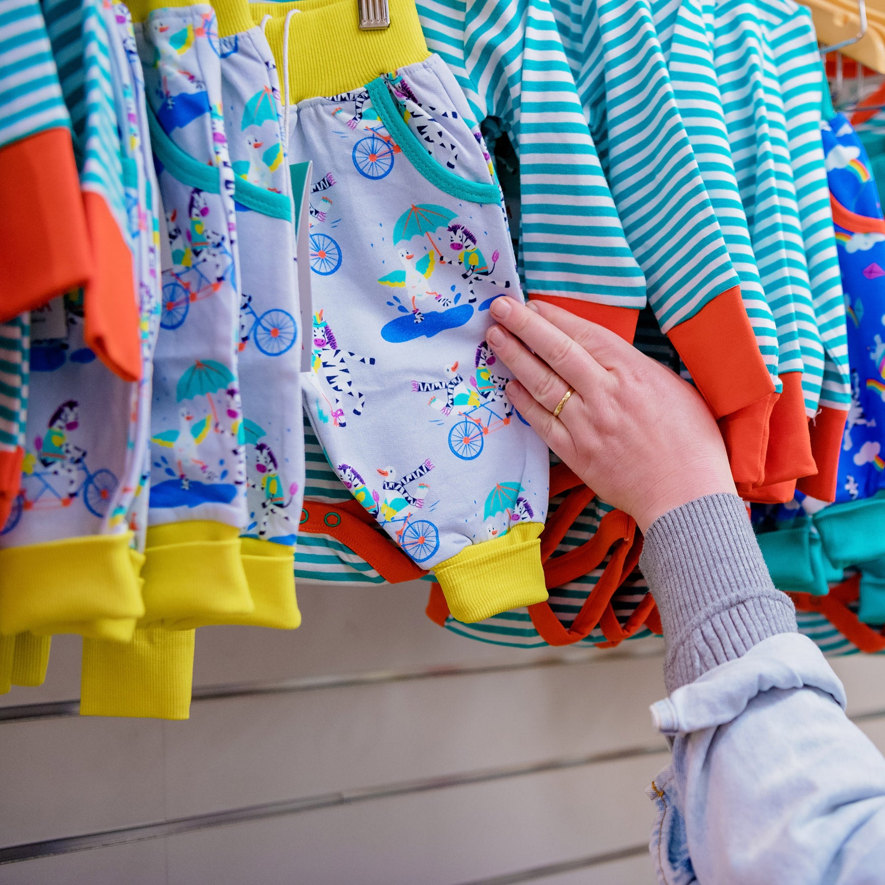 Colorful children's clothing on a rack with a hand selecting a piece.