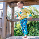Smiling boy running outside, wearing a long sleeve yellow and white stripe Ducky Zebra t-shirt with teal joggers with a repeat print pattern of campervans and paddleboards. The trousers have a turquoise cuff, which has been rolled up. The boy has bare feet.