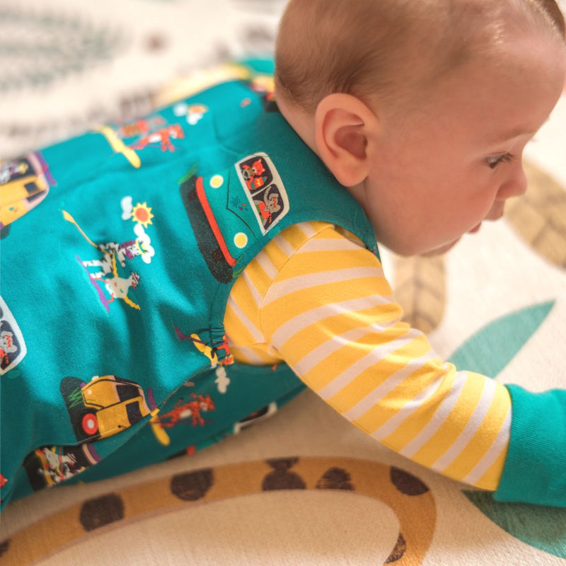 Baby lying on a patterned rug wearing a pair of Ducky Zebra teal dungarees with a yellow and white bodysuit below.