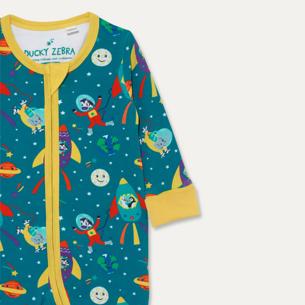 Close up image of a Ducky Zebra sleepsuit with a teal background and yellow trim and cuffs. The print has a zebra, elephant, duck and puffin dressed up in space outfits travelling through space.