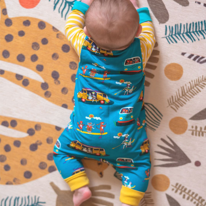 Baby lying on its front on a patterned rug. The baby is wearing a Ducky Zebra romper with paddleboards and campervans on the print. 