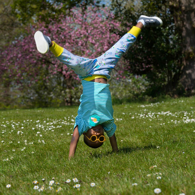 Image of a smiling child doing a handstand, while looking at the camera. They are wearing Ducky Zebra joggers and a Ducky Zebra turquoise stripe T-shirt