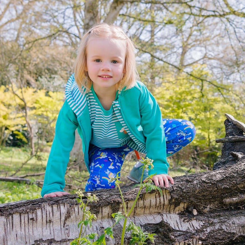 Image of a girl wearing an unzipped Ducky Zebra turquoise hoodie with a Ducky Zebra t-shirt and joggers - crouched outside by a fallen tree