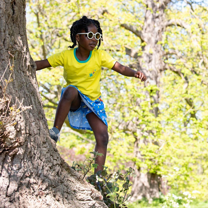 Image of a child, climbing a tree, wearing a Ducky Zebra skort, with the underneath shorts showing and a Ducky Zebra yellow t-shirt
