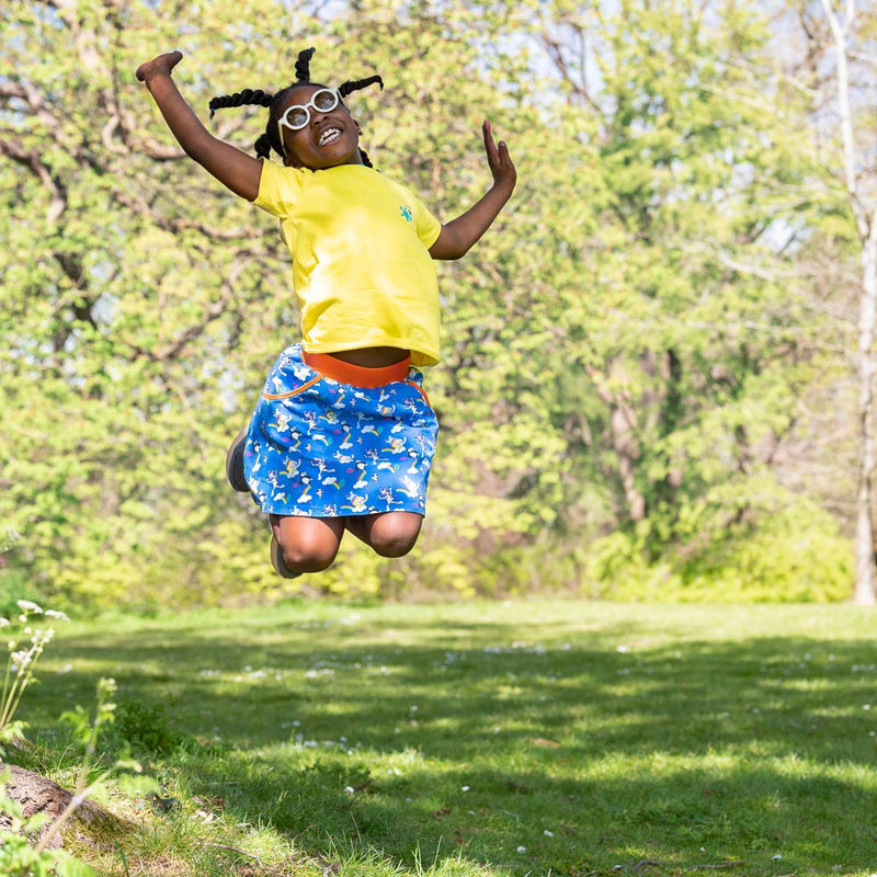 Image of a smiling child leaping in the air, wearing a bright yellow Ducky Zebra T-shirt and colourful Ducky Zebra organic cotton skort