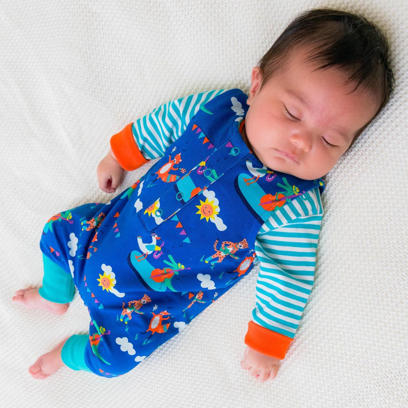 Image of a baby fast asleep wearing a Ducky Zebra sleeveless romper and long sleeve bodysuit. The dungarees have a repeat print pattern of a duck, crocodile, cheetah and fox playing in a festival.