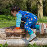 Image of a toddler climbing on a log wearing a Ducky Zebra sleeveless romper and long sleeve bodysuit. The dungarees have a repeat print pattern of a duck, crocodile, cheetah and fox playing in a festival.