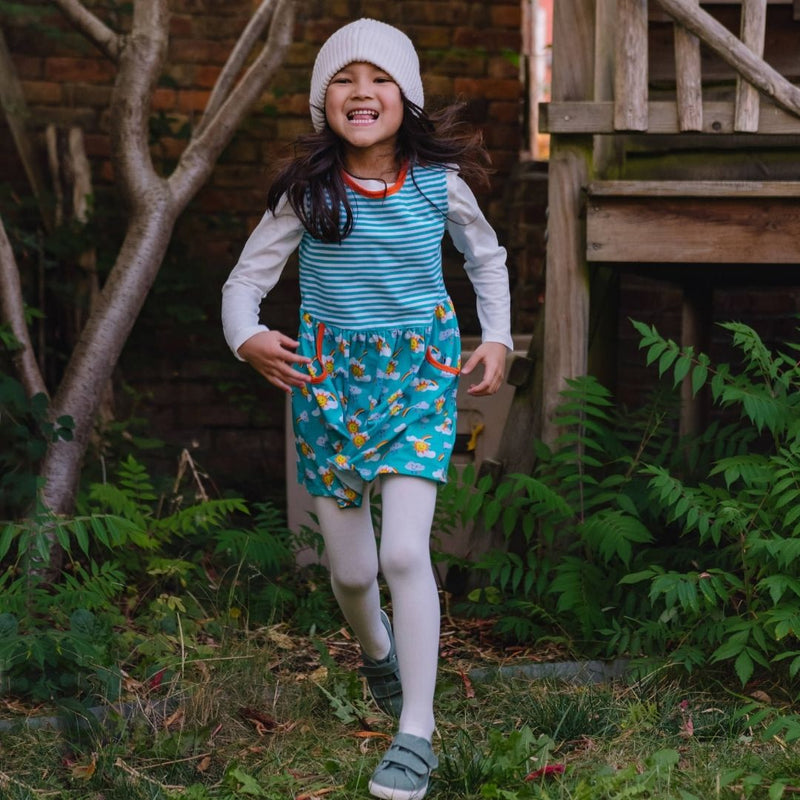 Image of a smiling girl, wearing a Ducky Zebra sleeveless dress with a long sleeve top underneath